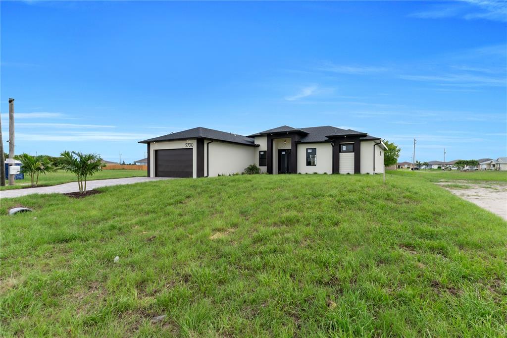 A modern, single-story house with a dark garage and white exterior sits on a lawn — 2720 SANTA BARBARA BOULEVARD N, CAPE CORAL, FL