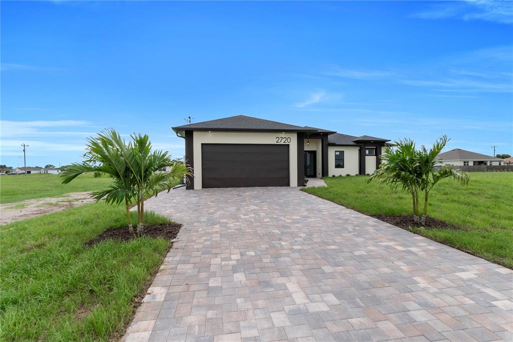 A modern single-story house features a paved driveway, a two-car garage, and two palm trees — 2720 SANTA BARBARA BOULEVARD N, CAPE CORAL, FL