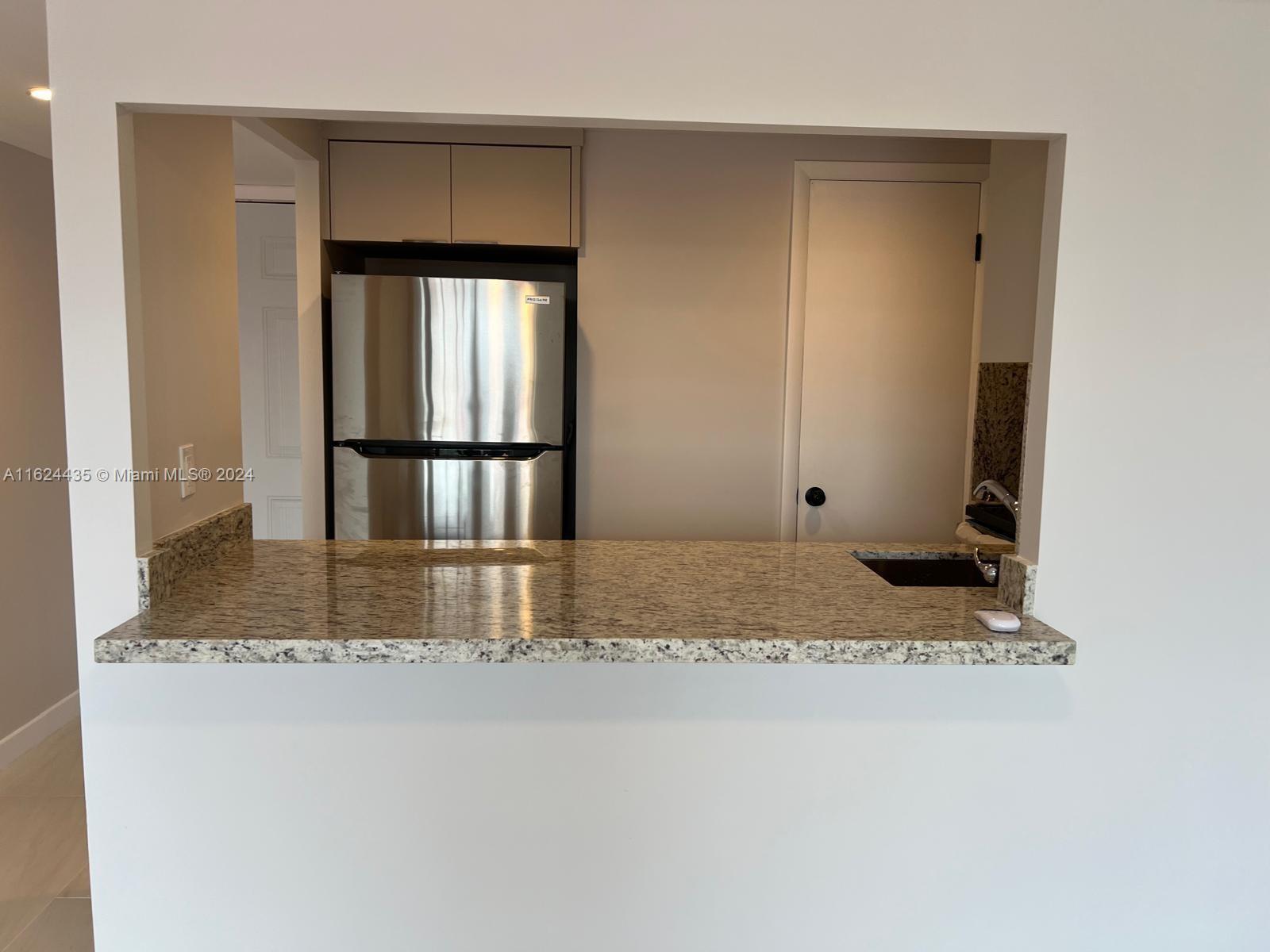 A kitchen pass-through features a granite countertop, stainless steel refrigerator, and light-colored cabinetry — 6580 W Flagler St # 309, Miami FL 33144, MIAMI, FL