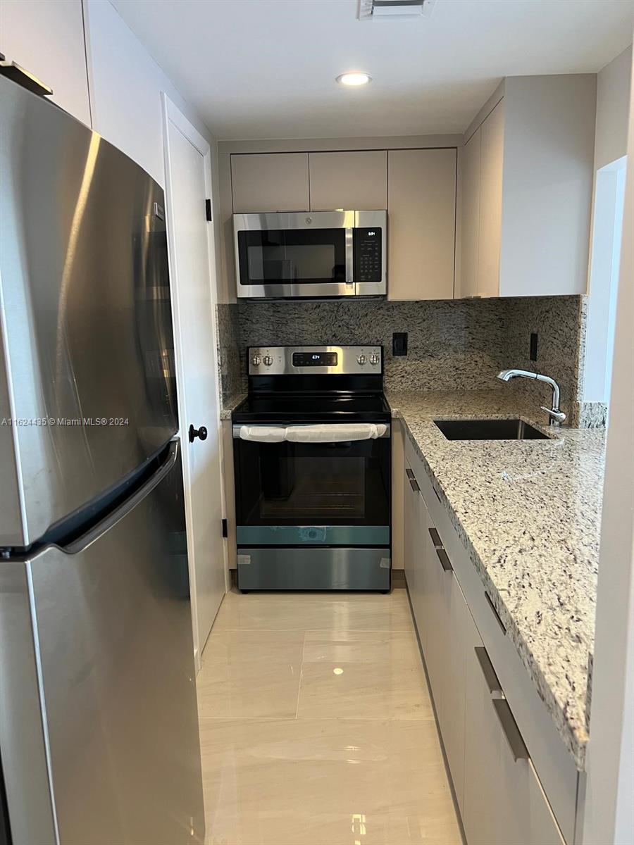 A galley kitchen features stainless steel appliances, granite countertops, and light-colored cabinetry — 6580 W Flagler St # 309, Miami FL 33144, MIAMI, FL