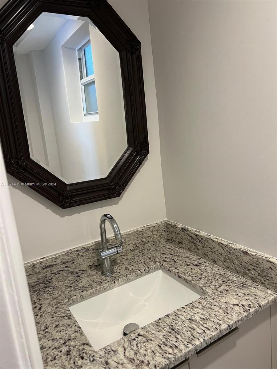 A bathroom features a granite vanity countertop, a white undermount sink, and an octagonal mirror — 6580 W Flagler St # 309, Miami FL 33144, MIAMI, FL