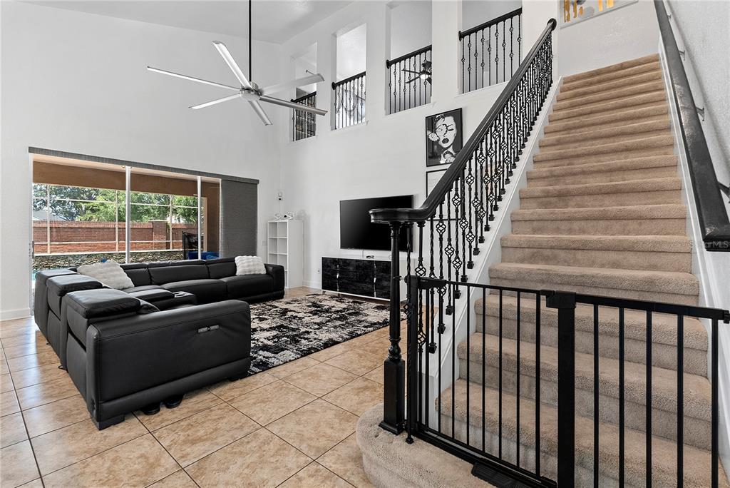 A living room features a black sectional sofa, a staircase with a gate, and tile flooring — 446 ANESSA ROSE LOOP, OCOEE, FL