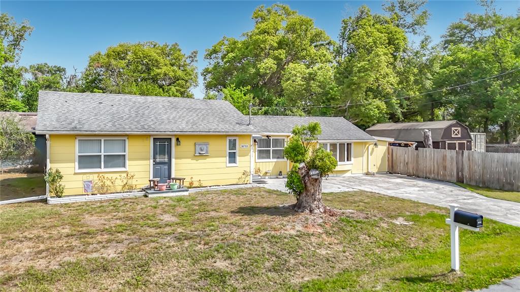A yellow single-story house with a gray roof, a paved driveway, and a wooden fence — 38703 9TH AVENUE, ZEPHYRHILLS, FL