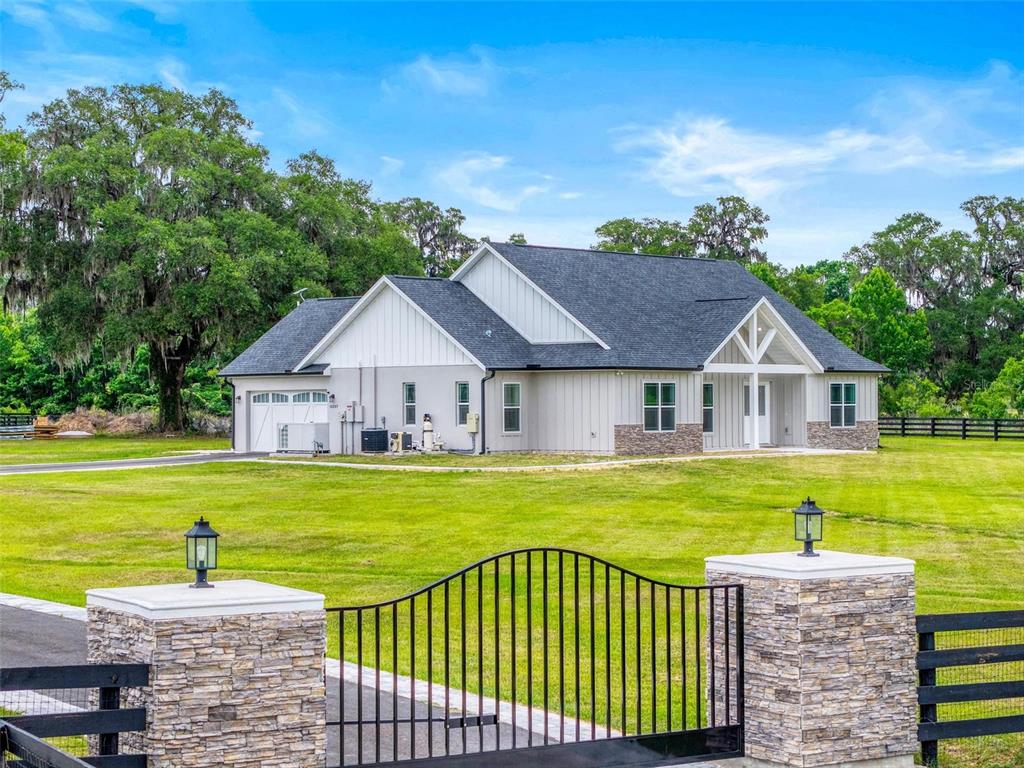 A modern farmhouse with a gray exterior and stone accents sits behind a gated entrance — 11257 NW 50TH LANE, OCALA, FL