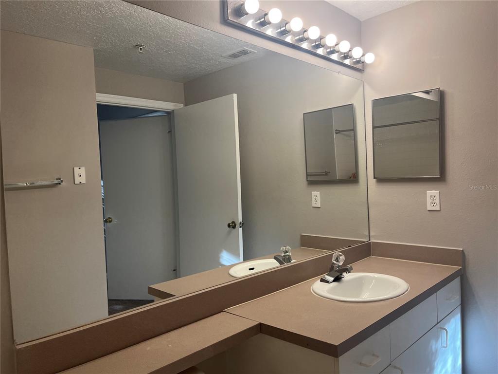 A bathroom vanity with a large mirror, dual sinks, and light-colored cabinetry — 5572 METROWEST BOULEVARD UNIT 209, ORLANDO, FL