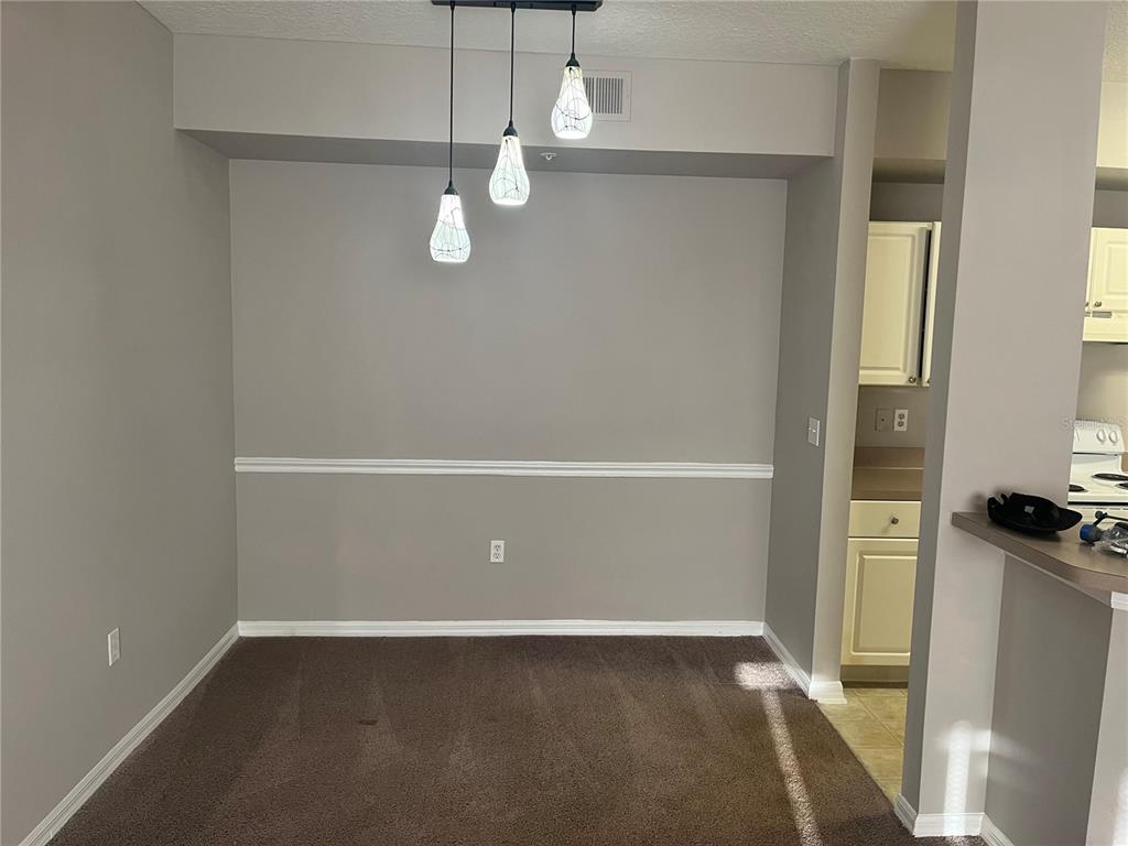 A dining area features brown carpet, gray walls with white chair rail molding, and pendant lighting — 5572 METROWEST BOULEVARD UNIT 209, ORLANDO, FL