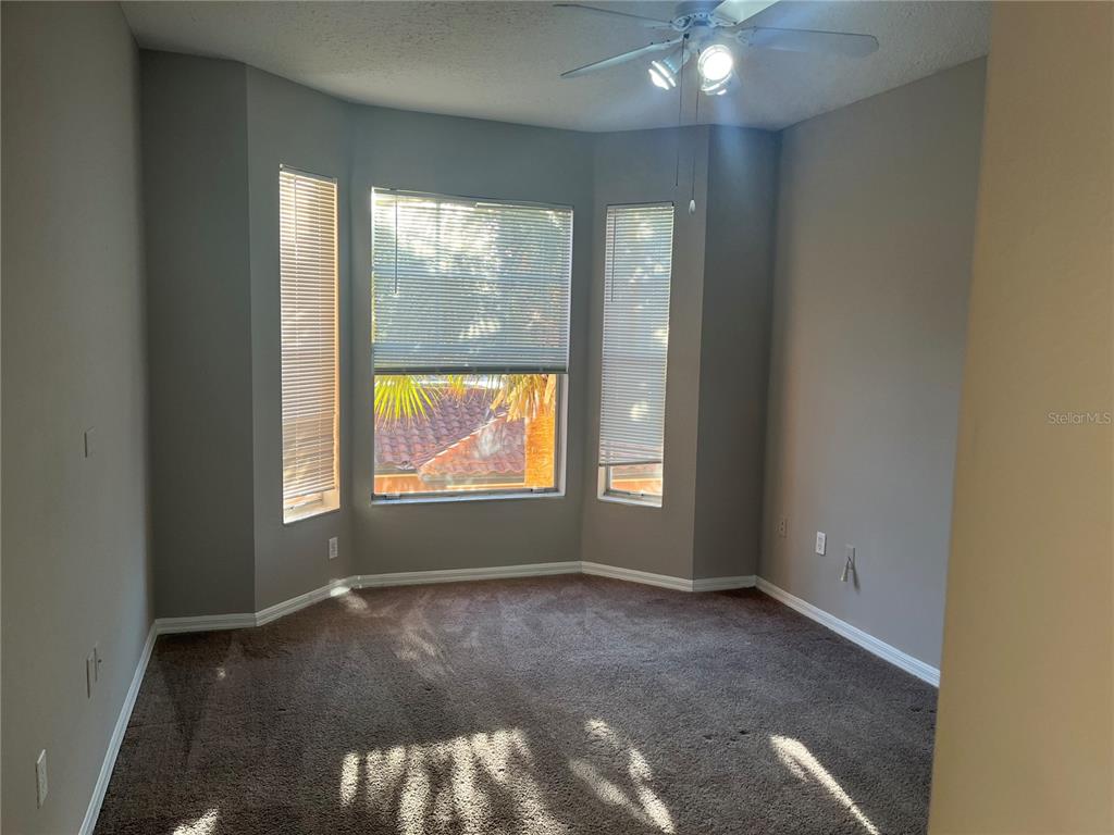 An empty bedroom features gray walls, brown carpet, a ceiling fan, and a bay window — 5572 METROWEST BOULEVARD UNIT 209, ORLANDO, FL