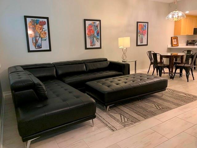 A living room features a black leather sectional sofa, a matching ottoman, and a dining area — 3401 54TH DRIVE W UNIT 103, BRADENTON, FL