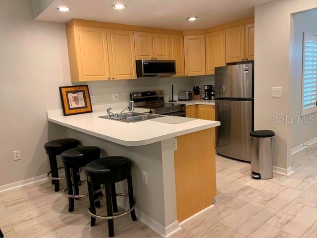 A kitchen features light wood cabinets, stainless steel appliances, and a breakfast bar with stools — 3401 54TH DRIVE W UNIT 103, BRADENTON, FL