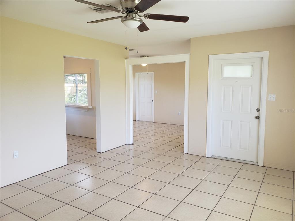 An interior view of a room with beige walls, tiled floors, a ceiling fan, and a door — 7475 19TH AVENUE N, ST PETERSBURG, FL