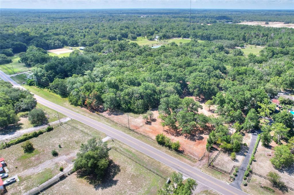 An aerial view shows a paved road running alongside a wooded lot with cleared areas — 11000 KITTEN TRAIL, HUDSON, FL