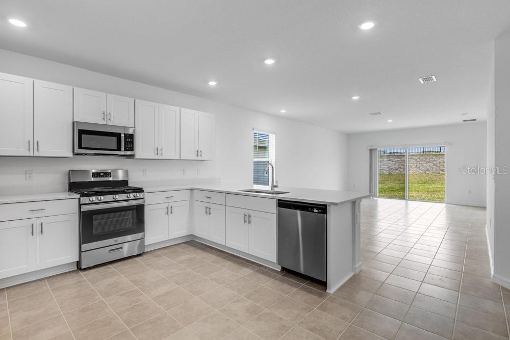 A kitchen with white cabinets, stainless steel appliances, and tile flooring opens to a living area — 13836 SHELLMORE AVENUE, PALMETTO, FL