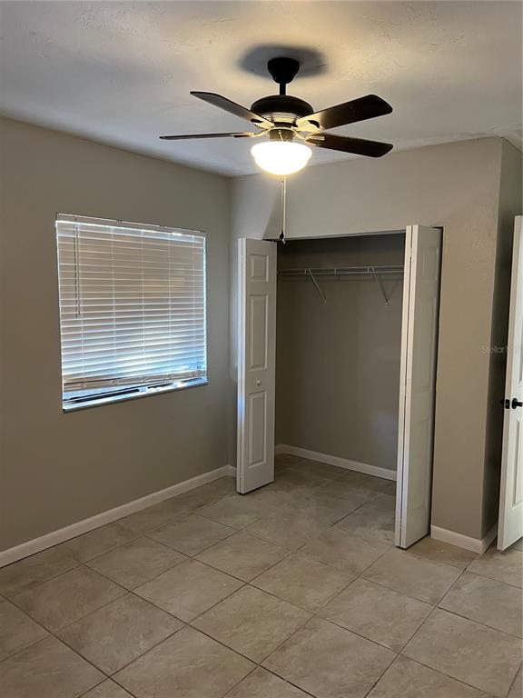 A bedroom with light gray walls, tile flooring, a ceiling fan, and an open closet — 1606 NW 20TH COURT, OCALA, FL