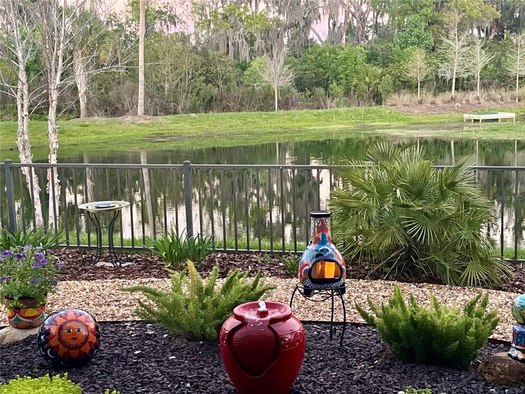 A backyard patio features a red water fountain, a decorative chiminea, and a pond view — 4193 SILVANA WAY, THE VILLAGES, FL