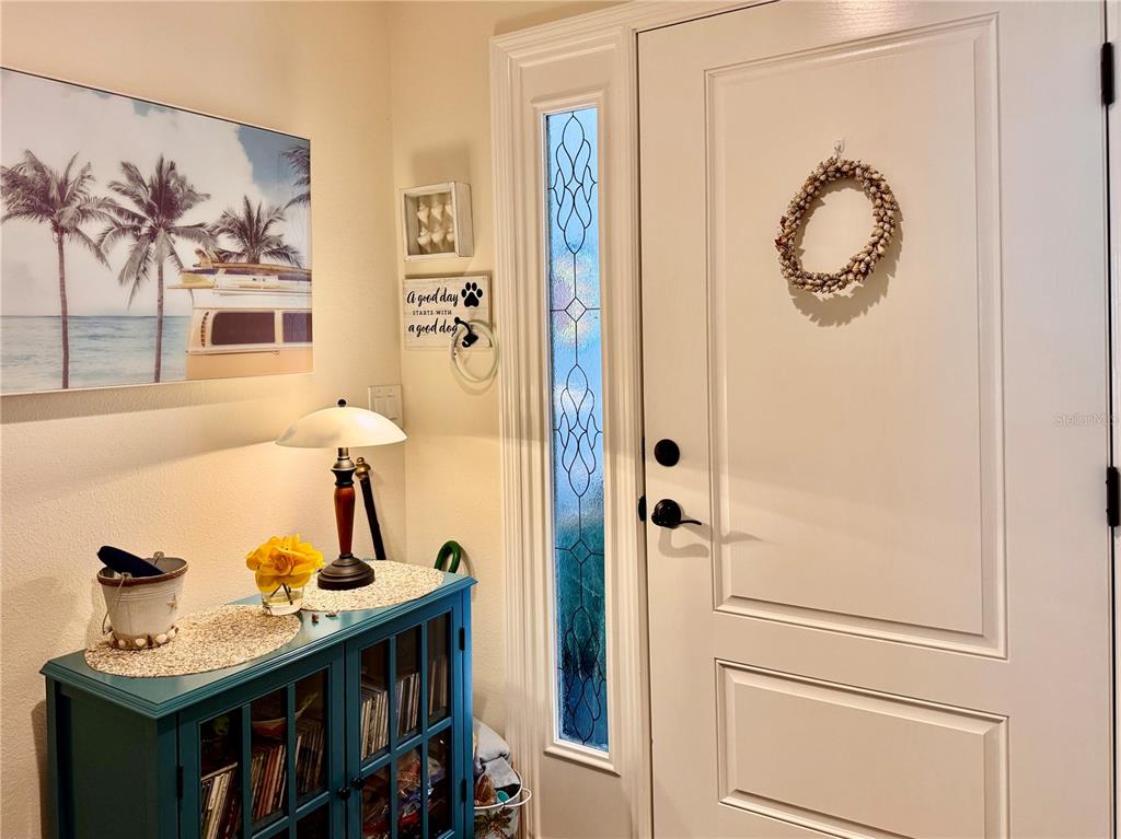 An entryway features a teal cabinet, a lamp, wall art, and a white front door — 4193 SILVANA WAY, THE VILLAGES, FL