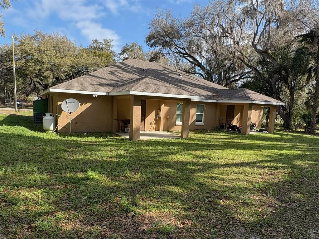 The rear exterior of a tan, single-story house features a covered patio and a satellite dish — 4300 W HIGHWAY 316, REDDICK, FL