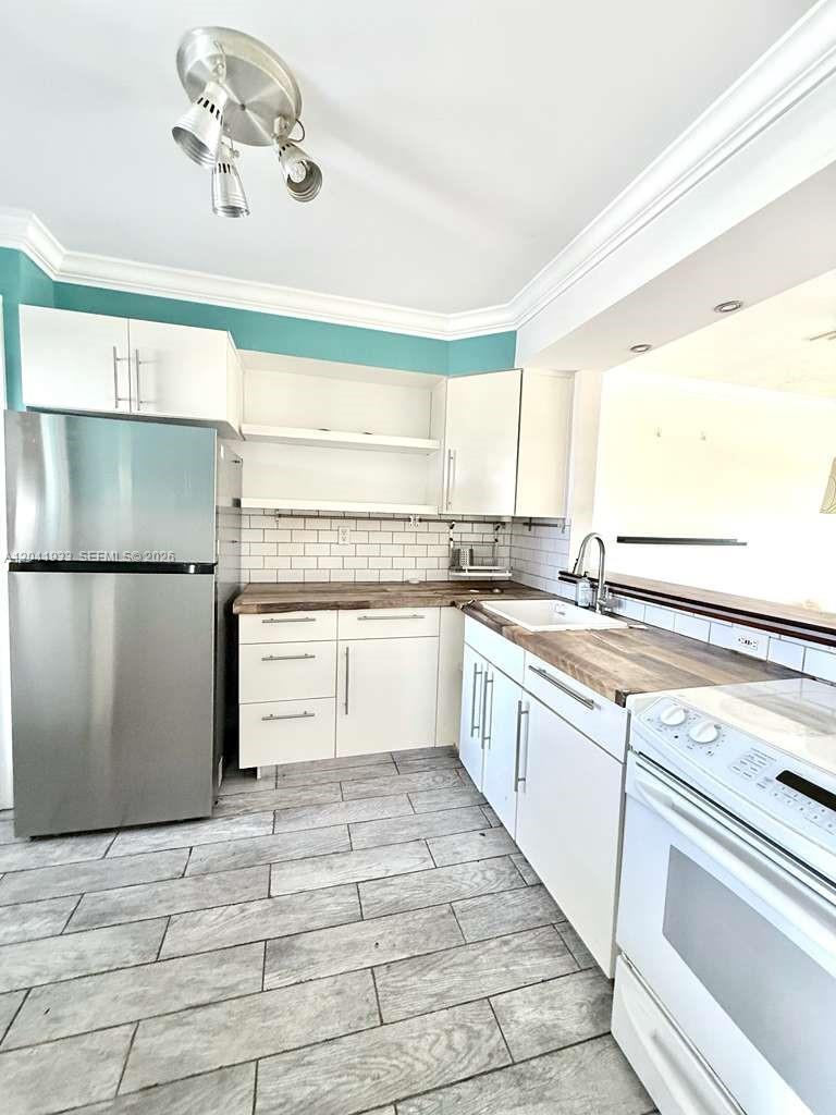 A kitchen features white cabinets, wood countertops, a stainless steel refrigerator, and gray tile flooring — 1530 NE 191st St # 340, Miami FL 33179, MIAMI, FL