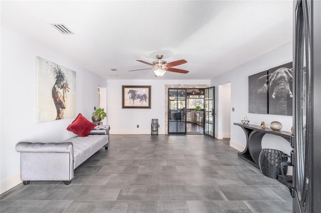 A spacious foyer features gray tile flooring, a tufted bench, and black-framed glass doors — 10310 GOPHER ROAD, HOWEY IN THE HILLS, FL