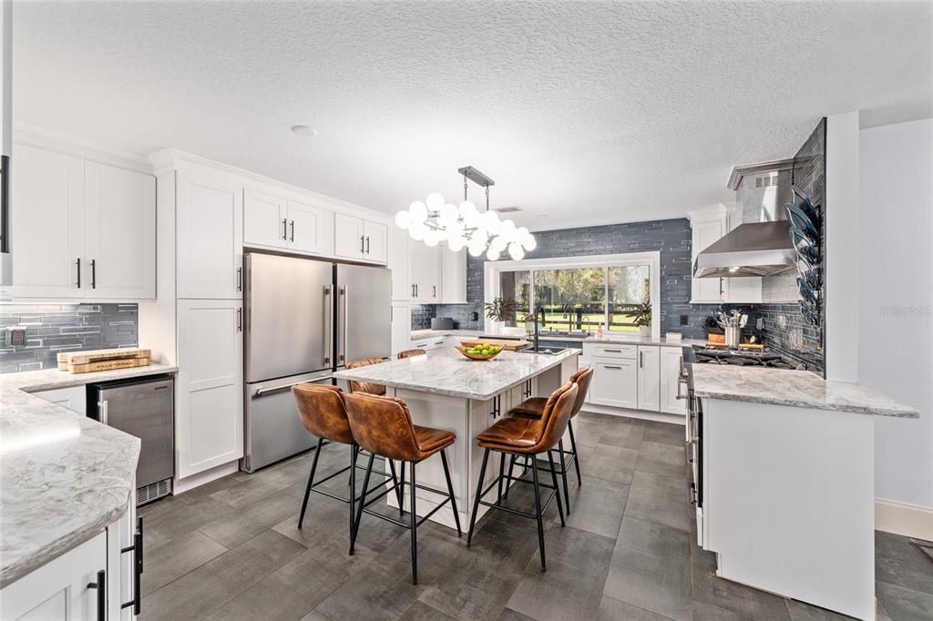 A modern kitchen features white cabinetry, a large marble-topped island, stainless appliances, and dark tile flooring — 10310 GOPHER ROAD, HOWEY IN THE HILLS, FL