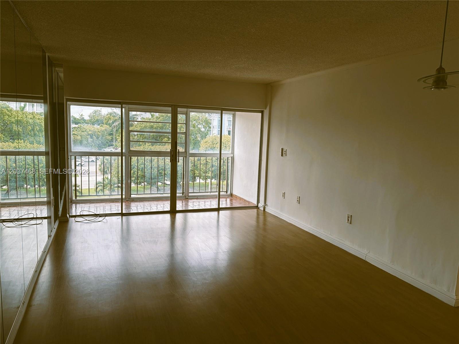 An empty room features wood-look flooring, a mirrored wall, and sliding glass doors to a balcony — 8775 Park Blvd # 406, Miami FL 33172, MIAMI, FL