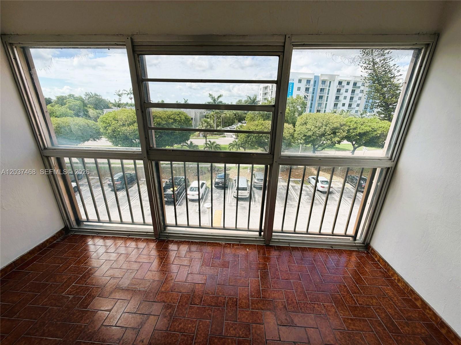 A sunroom features brown tiled flooring and large windows overlooking a parking lot and trees — 8775 Park Blvd # 406, Miami FL 33172, MIAMI, FL