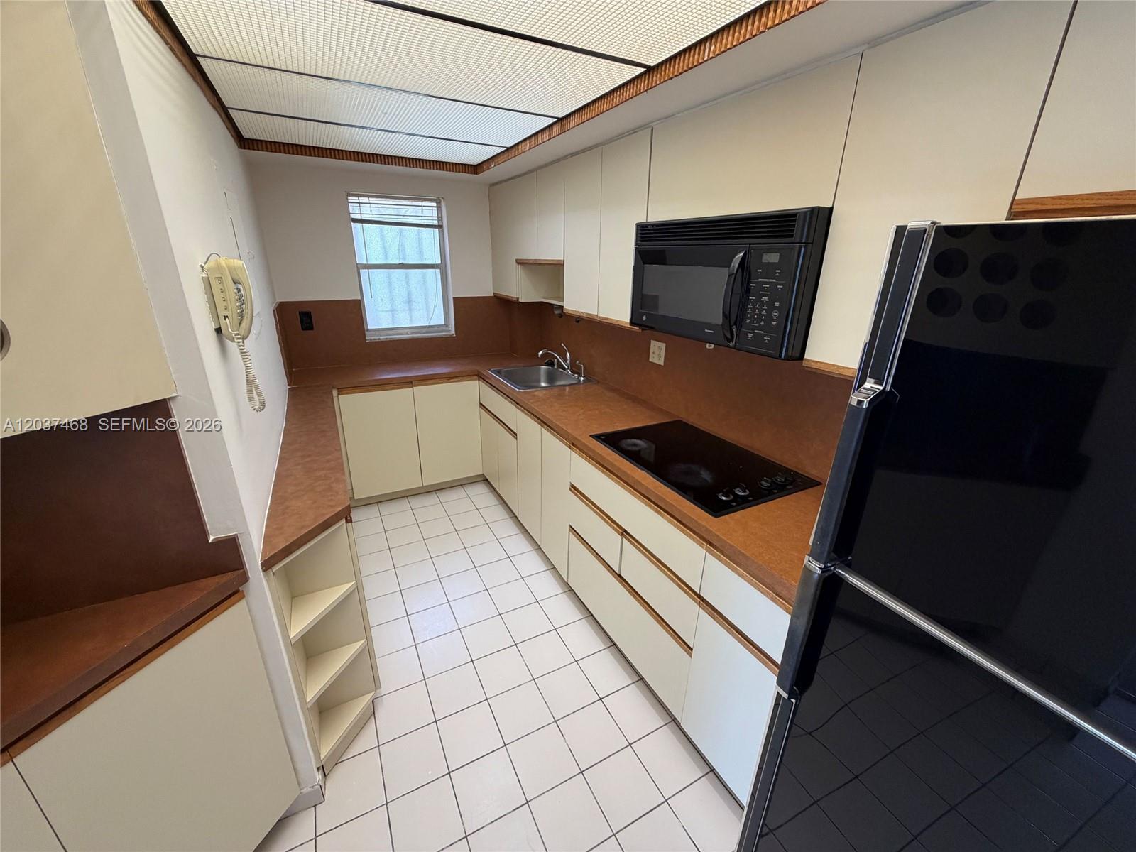 A galley kitchen features white cabinets, brown countertops, a black appliance suite, and tiled flooring — 8775 Park Blvd # 406, Miami FL 33172, MIAMI, FL