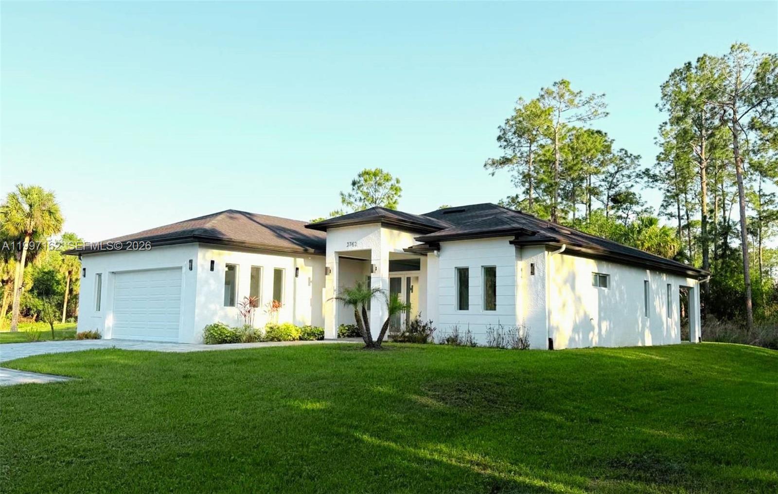 A white single-story house with a two-car garage sits on a grassy lawn — 3762 32nd AVE SE, Naples FL 34117, NAPLES, FL