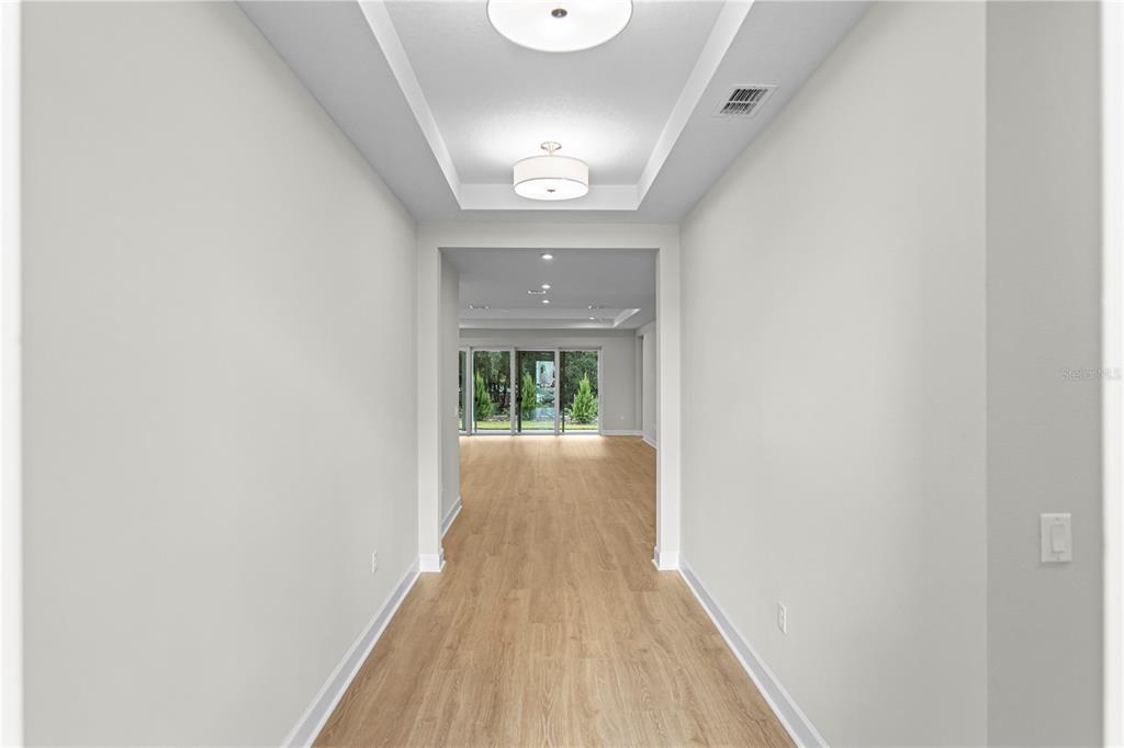 A hallway with light wood flooring leads to a living area with large glass doors — 956 CLUB CRESSWIND DRIVE, LADY LAKE, FL