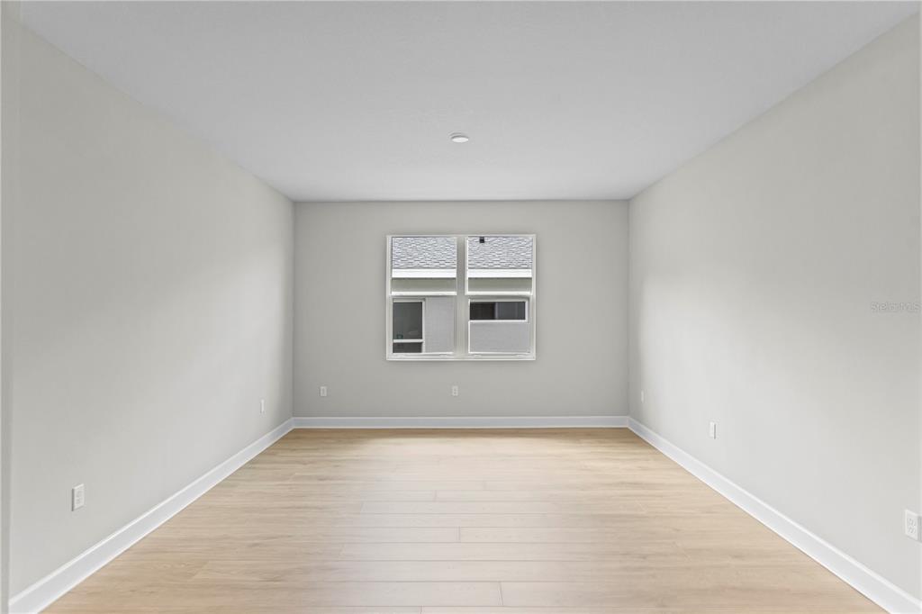 An empty room features light wood-look flooring, neutral walls, and a single window — 956 CLUB CRESSWIND DRIVE, LADY LAKE, FL
