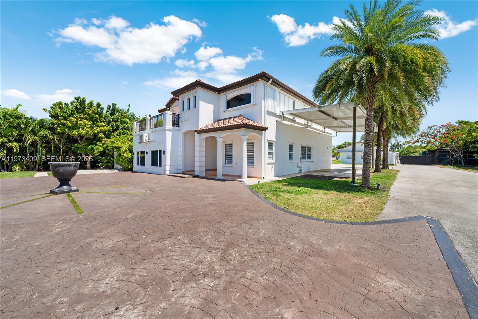 A two-story white house features a large paved driveway, a palm tree, and a carport — 13050 SW 26th St, Miami FL 33175, MIAMI, FL