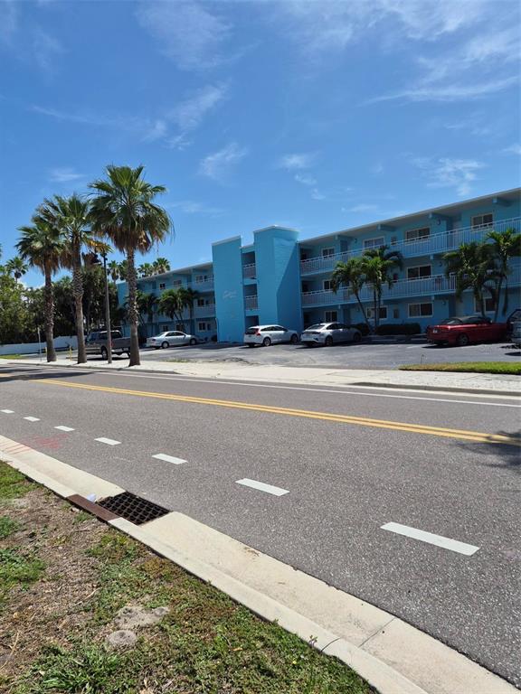 A multi-story blue apartment building stands behind a parking lot and a paved road — 1505 PASS A GRILLE WAY UNIT 17, ST PETE BEACH, FL