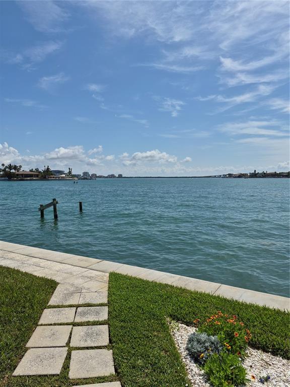 A stone walkway leads through a grassy lawn toward a waterfront view with wooden pilings — 1505 PASS A GRILLE WAY UNIT 17, ST PETE BEACH, FL