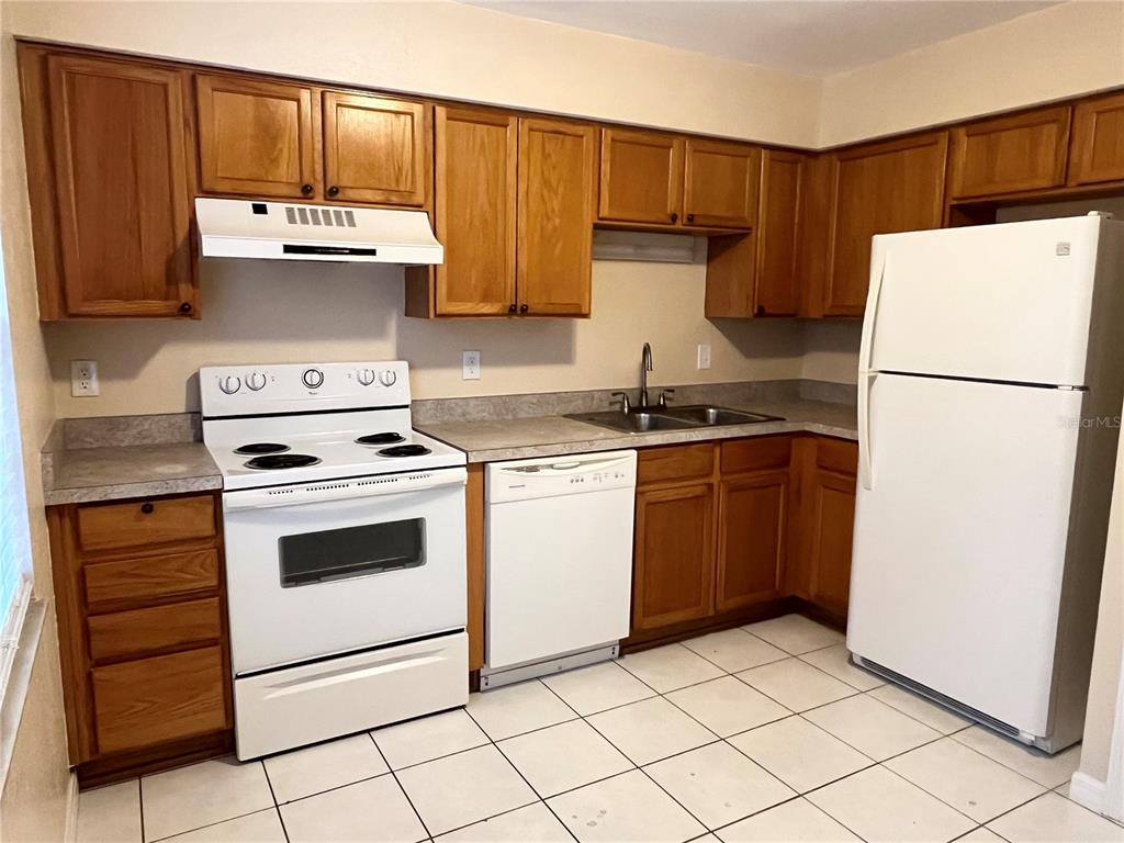 A kitchen features wooden cabinets, white appliances, a tiled floor, and laminate countertops — 37240 EMBASSY PARK LANE, DADE CITY, FL