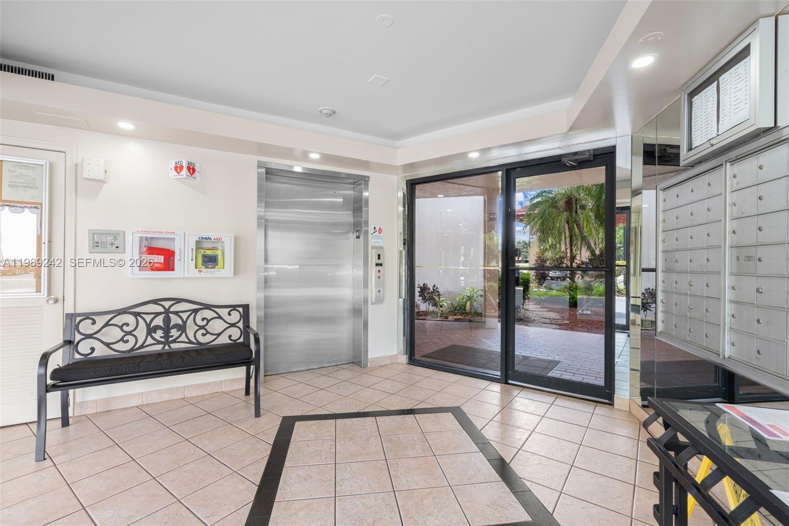 A building lobby features a metal elevator, a black bench, mailboxes, and glass entry doors — 3485 Environ Blvd # C205, Lauderhill FL 33319, LAUDERHILL, FL