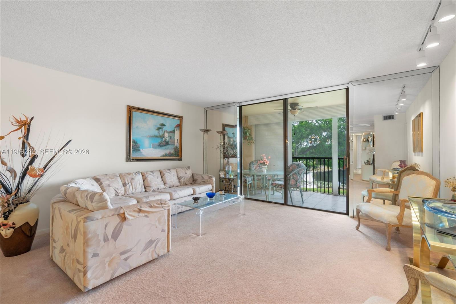 A living room features beige carpet, a floral sofa, glass coffee table, and sliding balcony doors — 3485 Environ Blvd # C205, Lauderhill FL 33319, LAUDERHILL, FL