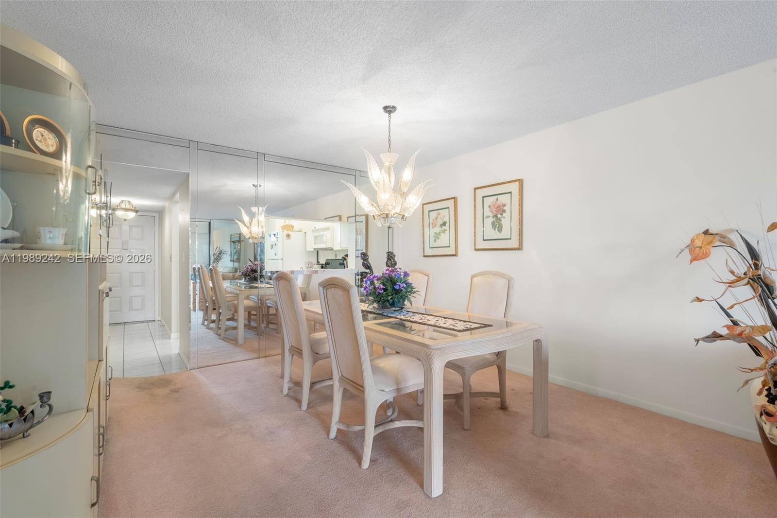 A dining room features a glass-topped table, upholstered chairs, a chandelier, and mirrored walls — 3485 Environ Blvd # C205, Lauderhill FL 33319, LAUDERHILL, FL