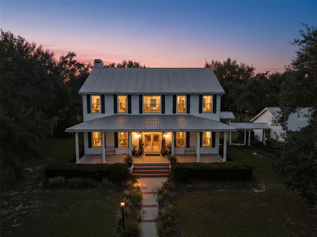 A two-story white farmhouse with a metal roof and a covered front porch at dusk — 23337 LAKE LINDSEY ROAD, BROOKSVILLE, FL
