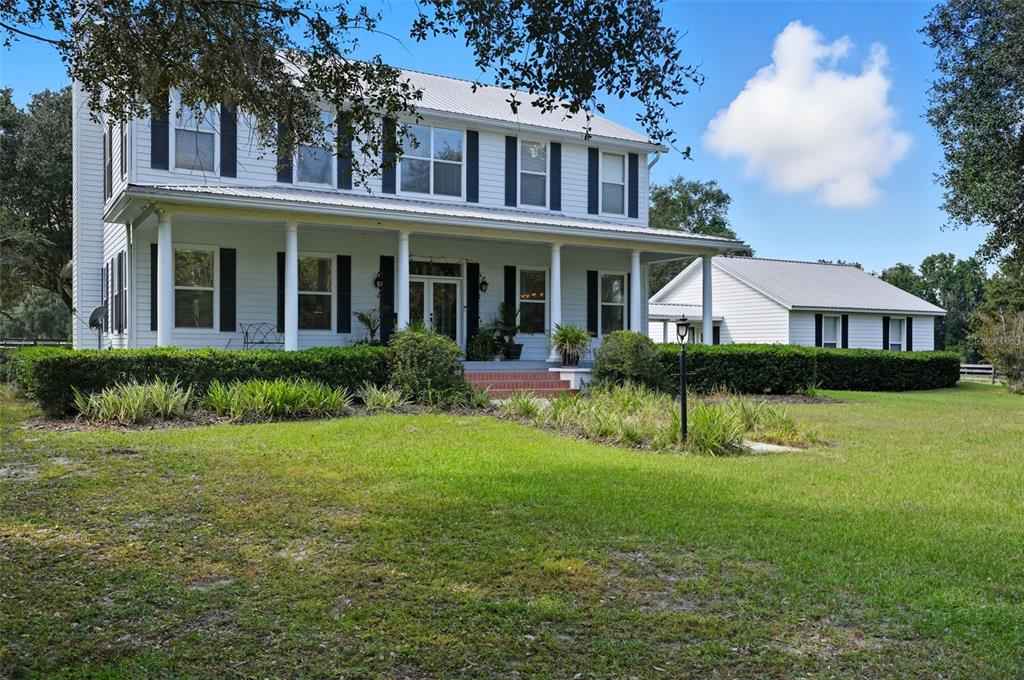 A two-story white farmhouse with a metal roof and a large front porch — 23337 LAKE LINDSEY ROAD, BROOKSVILLE, FL