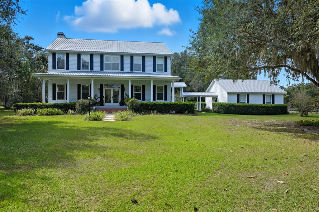 A two-story farmhouse with a metal roof and a detached garage connected by a breezeway — 23337 LAKE LINDSEY ROAD, BROOKSVILLE, FL