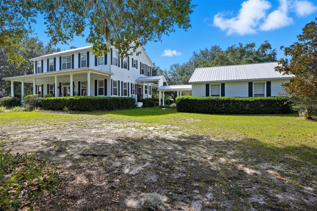 A white two-story farmhouse with a wrap-around porch and an attached garage — 23337 LAKE LINDSEY ROAD, BROOKSVILLE, FL