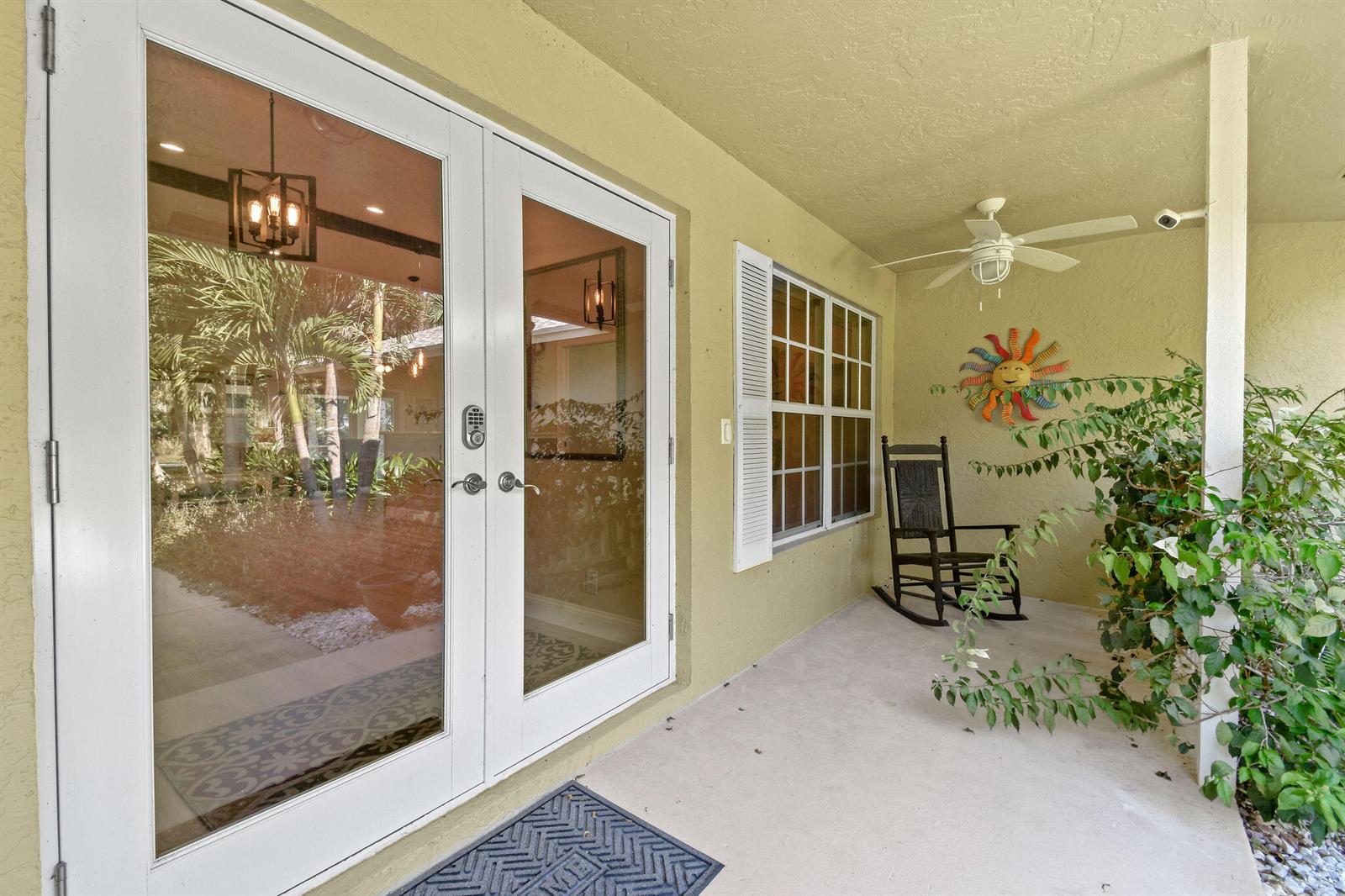 A covered porch features white French doors, a rocking chair, and a decorative sun wall hanging — 17861 Winterhawk Trail, FL 33478, FL