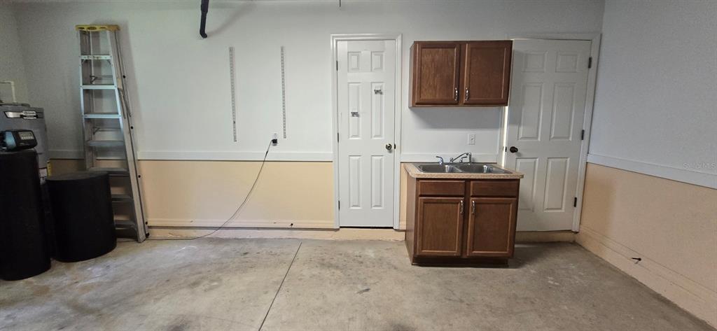 A garage interior features a utility sink, wooden cabinets, a ladder, and two white doors — 113 TEAK ROAD, OCALA, FL