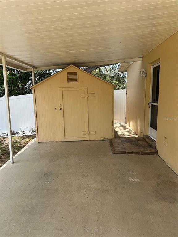 A covered concrete patio features a light-colored storage shed and an exterior door — 1117 NEWHOPE ROAD, SPRING HILL, FL