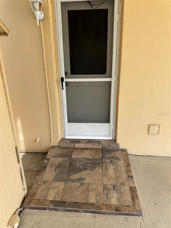 A tiled entryway leads to a white screen door on a tan exterior wall — 1117 NEWHOPE ROAD, SPRING HILL, FL