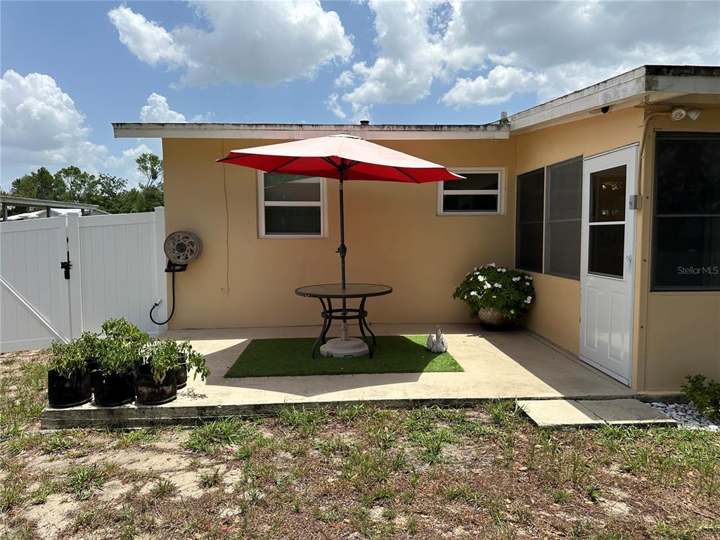 A patio with a table, red umbrella, and potted plants sits outside a tan house — 1117 NEWHOPE ROAD, SPRING HILL, FL