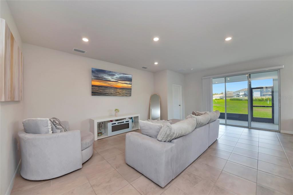 A living room features light-colored tile floors, a gray sofa, a swivel chair, and sliding doors — 627 160TH STREET E, BRADENTON, FL