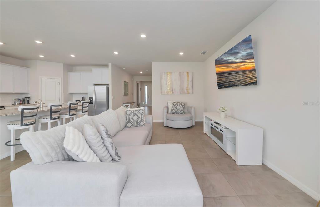 A living room features a white sectional sofa, a television, and an open-concept kitchen — 627 160TH STREET E, BRADENTON, FL