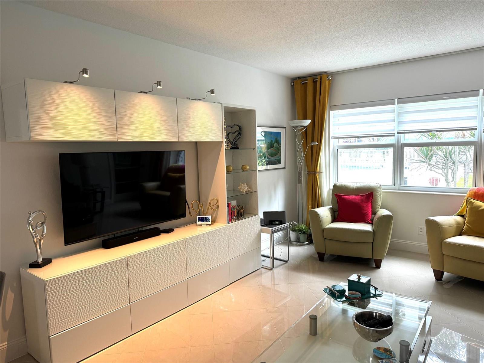 A living room features a large white media console, two armchairs, and a glass coffee table — 1481 S Ocean Boulevard # 124, Pompano Beach FL 33062, POMPANO BEACH, FL