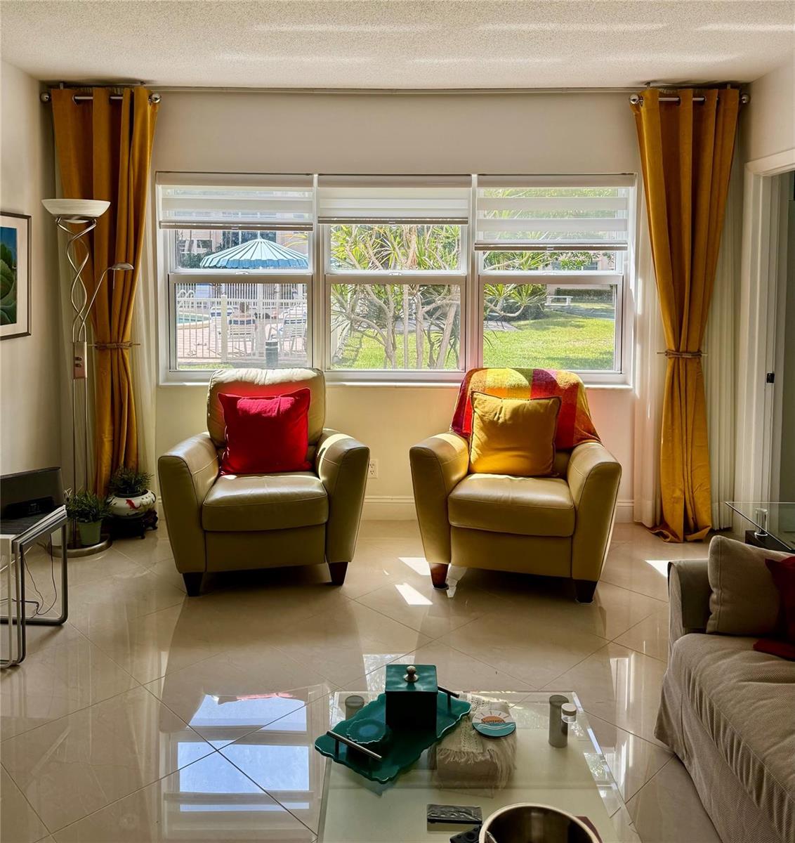 A living room features two leather armchairs, mustard curtains, and a view of a pool — 1481 S Ocean Boulevard # 124, Pompano Beach FL 33062, POMPANO BEACH, FL