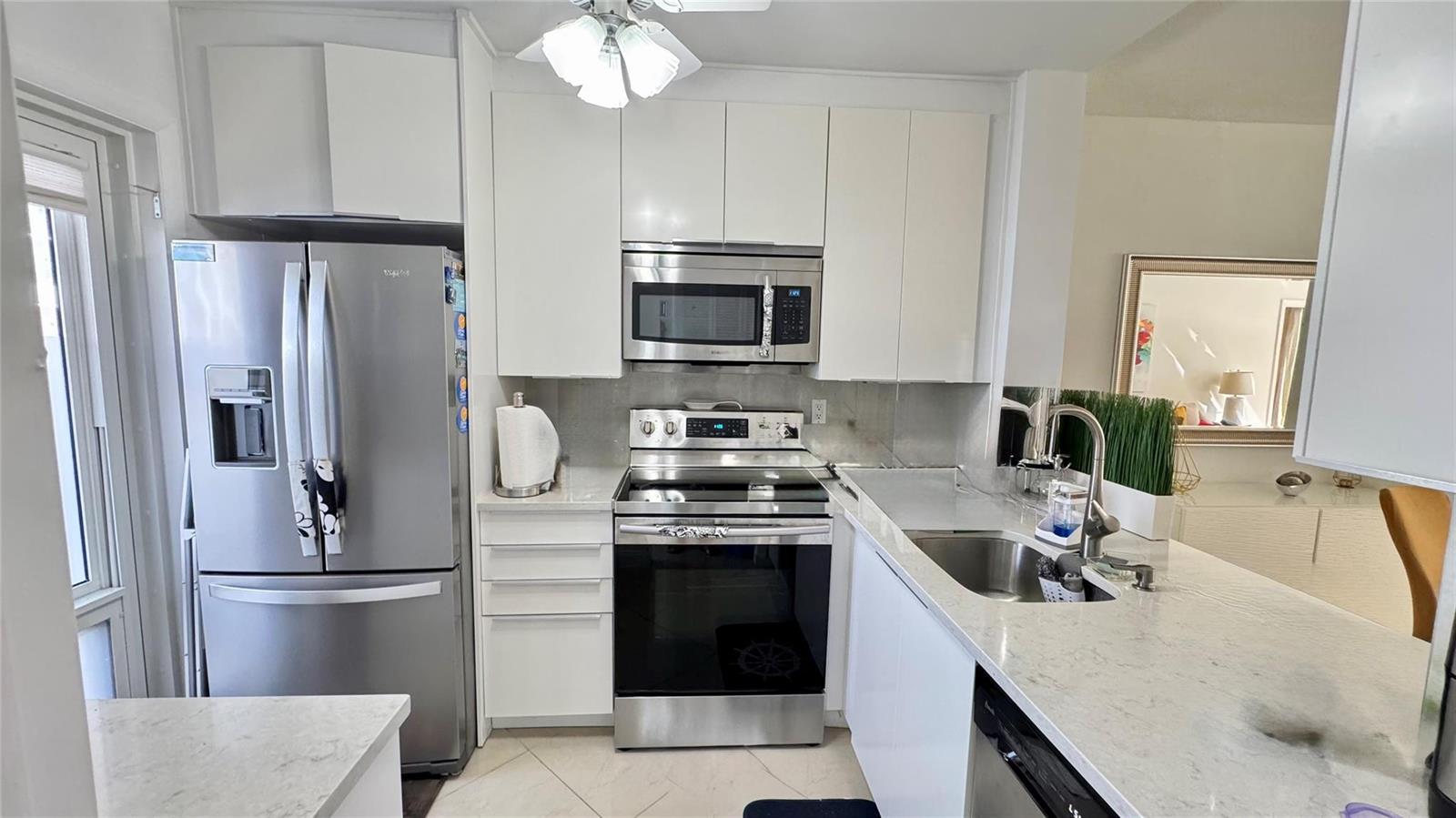 A kitchen features white flat-panel cabinets, stainless steel appliances, and light-colored stone countertops — 1481 S Ocean Boulevard # 124, Pompano Beach FL 33062, POMPANO BEACH, FL